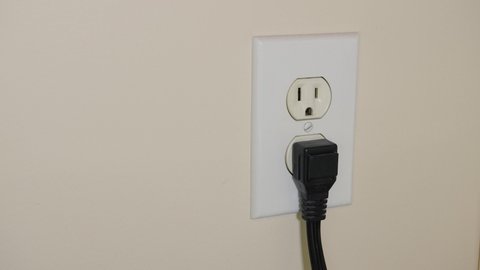 Close up of male hand unplugging electrical power cord from residential wall electricity outlet.