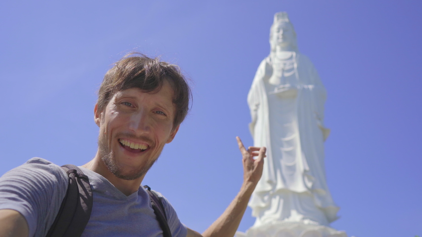 A young man tourist takes selfie video standing in front of the Son Tra Linh Ung Pagoda also known as Ledy Buddha in the city of Da Nang in central Vietnam. Travel to Vietnam concept