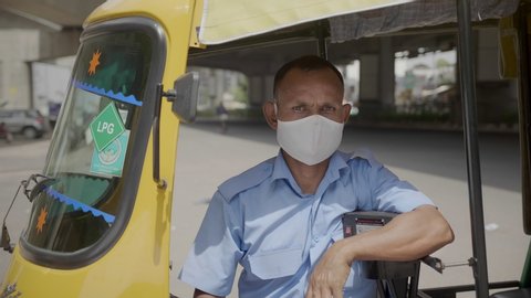 An Autorickshaw man sitting in a tuk tuk wearing face protective mask looking at the camera amid Coronavirus or COVID 19 epidemic or pandemic.