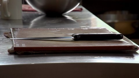 A sharp knife is setup ready on a chopping board in a professional kitchen setting. reflections of staff walking around.