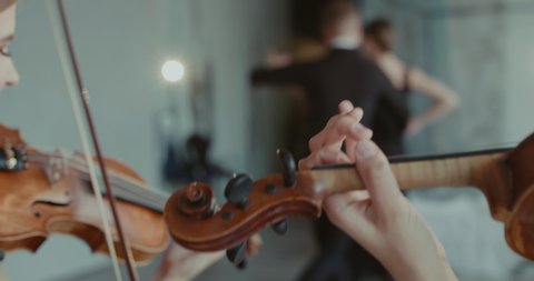 Close view of musicians playing the violins on blurred background of dancers performs passionate ballroom dance in studio. Slowly in 4K