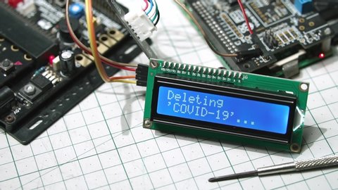 Closeup, Blue LCD display screen connected with computer board and circuit, showing "Deleting Covid-19", "Loading New Normal" and "Completed" word. Fight Covid-19 with technology & New normal concept.