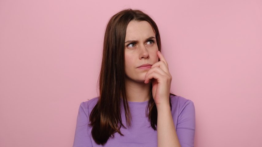 Portrait of thoughtful confused young woman touching chin, scratching head while thinking over solution, brunette girl having doubts about difficult choice, isolated on pink studio background Royalty-Free Stock Footage #1057069715