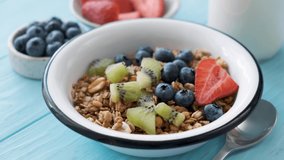 Pouring milk in bowl with granola and fruits. Preparing healthy breakfast food.