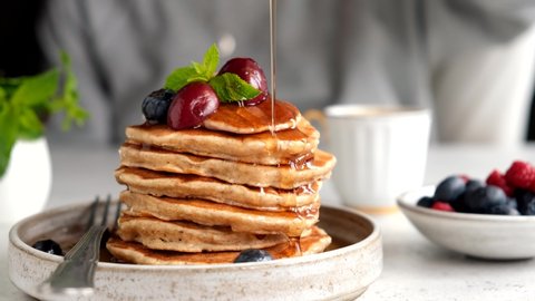 Pouring syrup on pancakes. Stack of american buttermilk pancakes with berries and maple syrup. Tasty sweet breakfast food