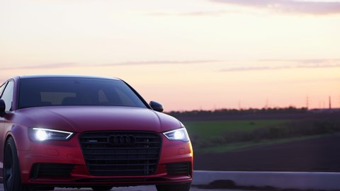 Dnipro/Ukraine 04.10.2020
Powerful red sports car, tuned matte Audi at sunset, smooth lines of body of elegant vehicle. pasting car with red matte protective film, driving on empty road, setting sun.