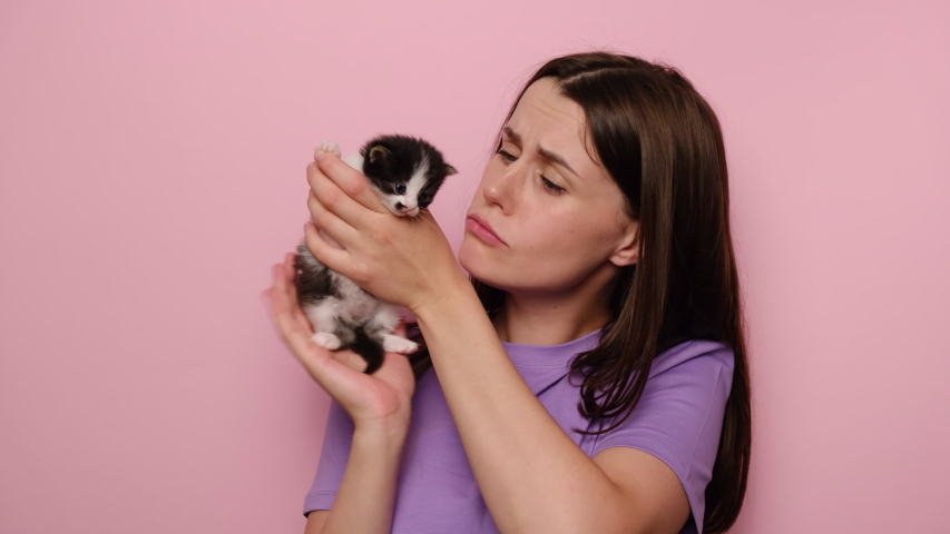 Cheerful attractive young woman with cute little pet cat looking at camera, isolated on pink studio background with copy space. Positive human emotions, facial expression, feelings