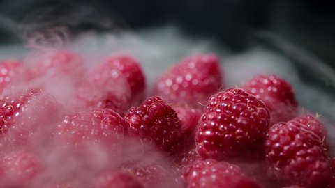 Ripe chilled red raspberries with dry ice steam isolated on dark background. Dieting, vitamins, antioxidants concept. View of delicious dessert.