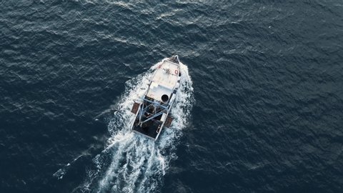 Fishing boat flying drone with large catch fish swirling hungry gulls flock of glaruses aerial view drone slow motion. Small ship floats on sea surface leaving path of sea foam water. Top view