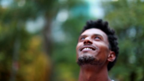 Mixed race man looking to the sky outside, close-up african descent person feeling hopeful smiling.