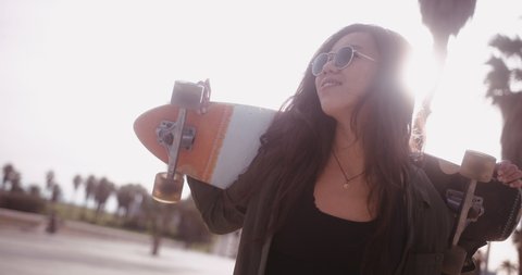 Young Asian hipster woman with skateboard walking in city