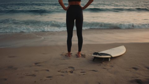 Surfer girl standing and looking at Pacific ocean, getting ready for a surfing training, camera moving in from back