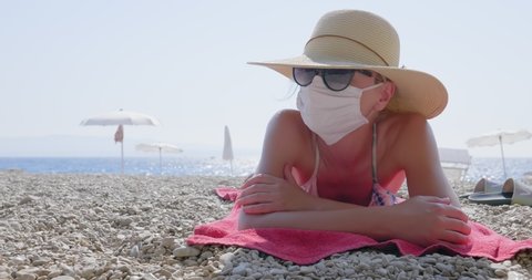 A woman with a hat and a medical mask is lying on the beach. She keeps a social distance because of the corona virus. Famous Golden Horn beach (Zlatni Rat) in Croatia.
