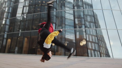 Young male and female athletes in sportswear performing aerial cartwheel and side flip while practicing parkour tricks together outdoors in the city