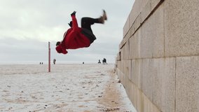 Slow motion shot of young man in sportswear and neck warmer running straight up the wall and doing backflip while practicing parkour outdoors on winter day - Powered by Shutterstock - Get 15% off with code: PIKWIZARD15
