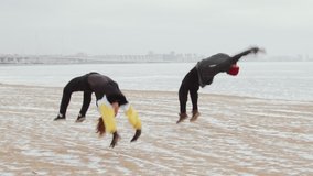 Slow motion shot of young athletic man and woman in sportswear performing cartwheel and backflips together while doing parkour on snowy lakeshore on winter day - Powered by Shutterstock - Get 15% off with code: PIKWIZARD15