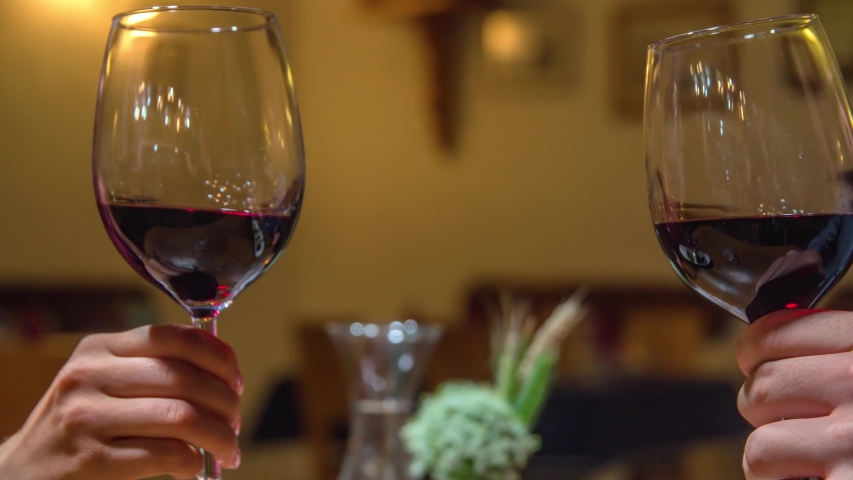 Couple is clinking wine glasses filled with red wine, slow motion