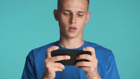 Attractive excited guy intently playing in game on smartphone over colorful background