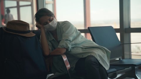 A young woman in a facial protective mask sleeping at the airport lounge while waiting for her flight.