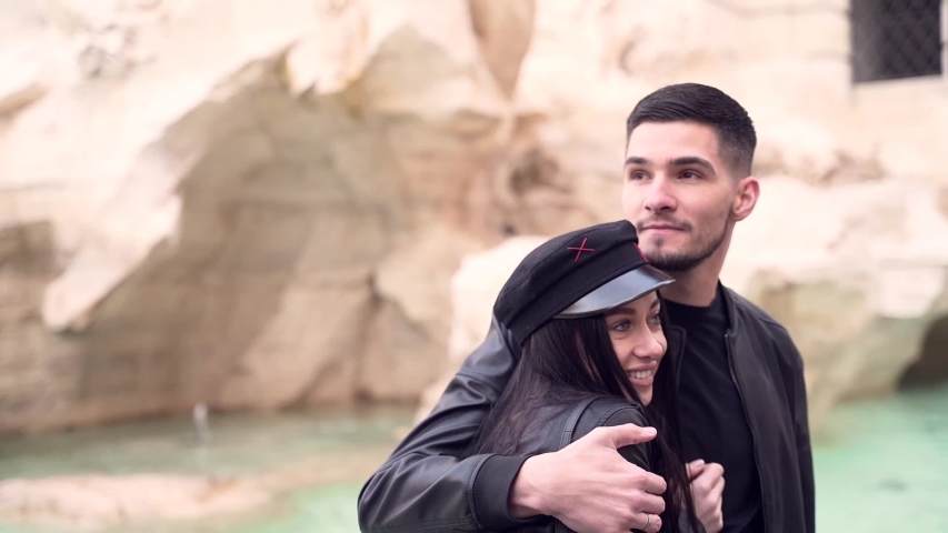 Portrait of a pretty couple of young people in love in black clothes. leather jacket, cap. Against the background fountain. Man and woman tourists hugging on the outside. Stylish hipsters together