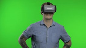Amazed man using VR app headset helmet to play simulation game, drawing. Watching virtual reality 3d 360 video. Isolated on chroma key green background in studio. Guy in VR goggles looking around