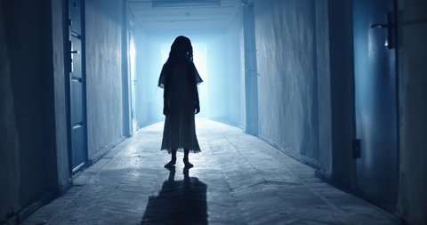 Little girl in white dress looking like a ghost slowly creeping down the hallway of a haunted house - halloween costume party, horror movie 4k footage