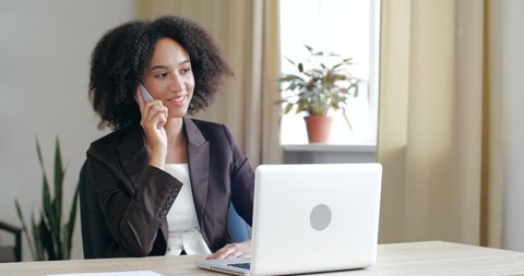 Young friendly business woman consultant wearing blazer jacket, sitting in cozy office at home, talking on mobile phone line, speaking negotiating, discussing with people, answering call positivly