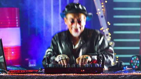 Funny elderly Grandpa DJ having fun in a nightclub. Funny moments with old men. Club DJ playing mixing music on the vinyl turntable at the party.