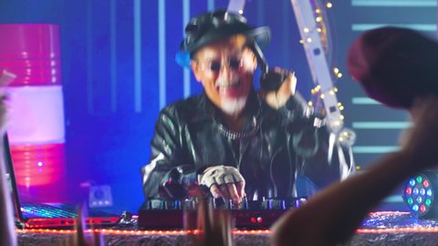 Funny elderly Grandpa DJ having fun in a nightclub. Funny moments with old men. Club DJ playing mixing music on the vinyl turntable at the party.