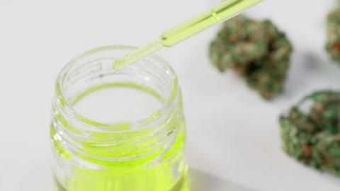 Close up of a pipette dropping medical cannabis oil into a glass with marijuana buds around shot in 4k super slow motion