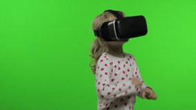 Child teen girl puts on VR headset helmet to play simulation app game. Watching virtual reality 3d 360 video. Isolated on chroma key green background in studio. Kid using VR goggles looking around