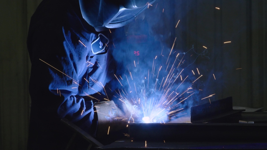 Dramatic shot of Man Welding in USA Factory Working with Steel in Classic Blue Collar American Job