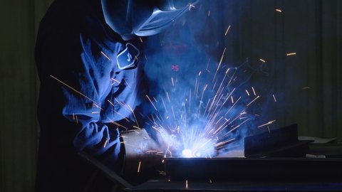 Dramatic shot of Man Welding in USA Factory Working with Steel in Classic Blue Collar American Job