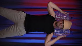 Vertical video.Man performs back squats using large bottles of water as a weight.Training at home during quarantine.Home Workout.Red-Blue background.Ready for stories.
