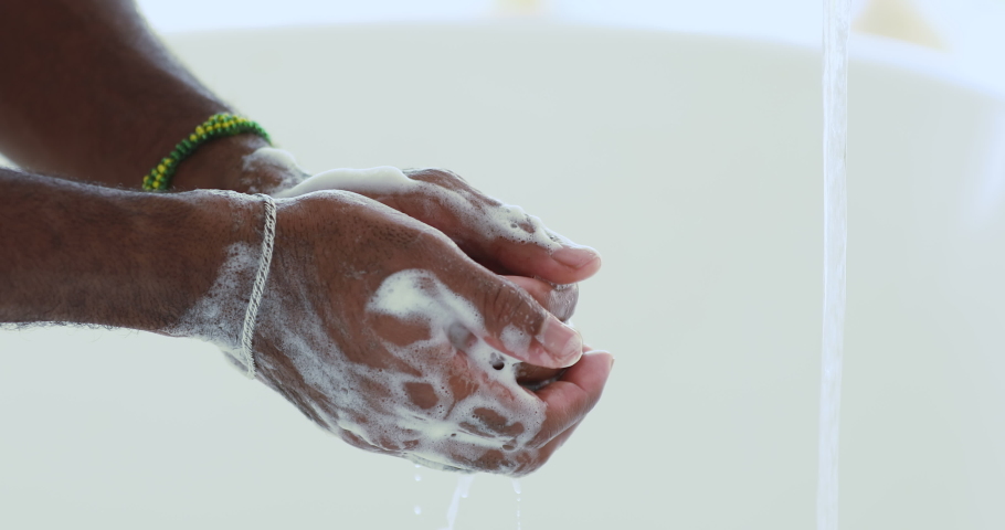 Close up young african ethnicity man washing hands with bubble soup. Mixed race guy rubbing hands with sanitizer, rinsing under running tap water, stop spreading coronavirus covid19 infection. | Shutterstock HD Video #1057121870