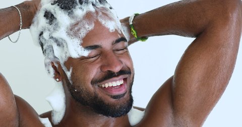 Head shot close up happy relaxed handsome african ethnicity man cleaning head with bubbles shampoo. Smiling young biracial guy enjoying washing hair with deep cleansing gel, morning hygienic routine.