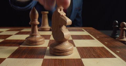 Close up of grandmaster hand moving white knight on board during chess game. Businessman making tricky move playing chess. Business leader and confrontation concept