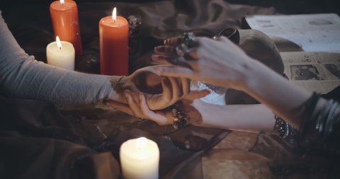 Close up of fortune teller woman point her finger to another woman palm reading her future. Female hand in hands of psychic over table with burning candles