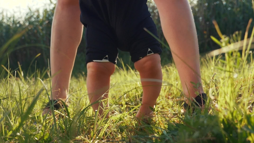 Baby takes first steps in grass. mom walks with son in nature kid dream concept. baby takes first steps with mom. mom and little son feet baby close-up happy family | Shutterstock HD Video #1057132724