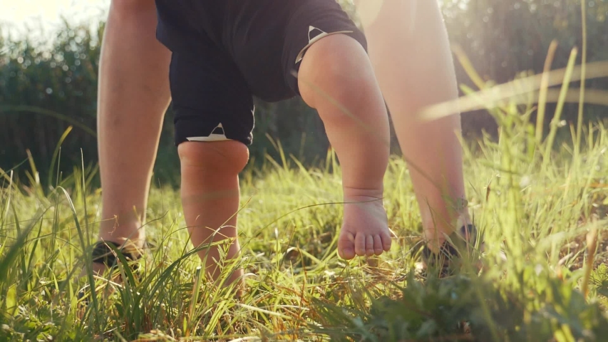 Baby takes first steps in grass. mom walks with son in nature kid dream concept. baby takes first steps with mom. mom and little son feet baby close-up happy family | Shutterstock HD Video #1057132724