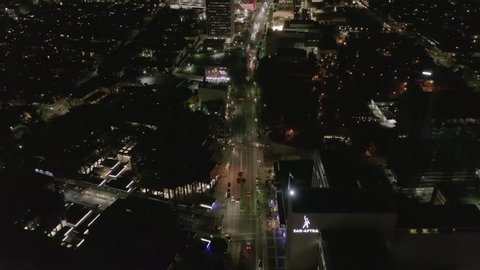 AERIAL: Over Wilshire Boulevard in Hollywood Los Angeles at Night with Glowing Streets and City Car Traffic Lights 
