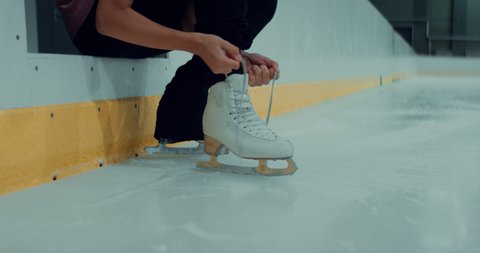 Professional teenager boy figure skater tying laces on skates before training on indoor ice arena. Shot on RED cinema camera with 2x Anamorphic lens, 75 FPS Slow motion