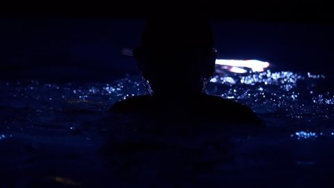 Silhouette of a child playing in dark water illuminated by blue light, in slow motion