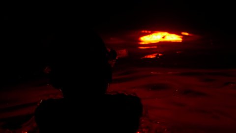 Silhouette of a child playing in dark water illuminated by red light, in slow motion