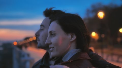 Close-up portrait of a beautiful young couple on the street of the night city against the background of colorful lights. Love story, romantic atmosphere. Two lovers hug and watch the sunset. Slow