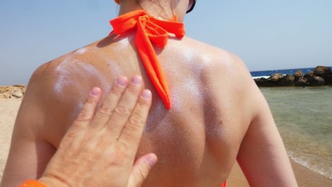 close-up, male hand applies sunscreen or spray lotion to skin of female back. on the beach under the hot sun, against the backdrop of the sea. Sun and UV protection. skin protection