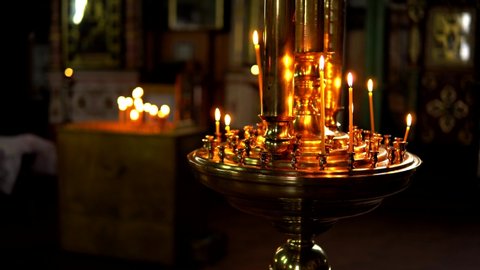 Gold large candlestick with burning candles on a blurred background of the dark room of the Orthodox Church. Theme religious faith and God, culture and traditions of Orthodoxy.