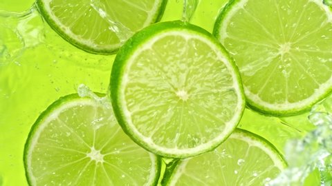 Super Slow Motion Shot of Lime Slices Falling into Water on Green Background at 1000fps.