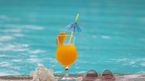 close up fresh juice orange cocktail, flower orchid and sunglasses on background blue water swimming pool. relaxing vacation happy holiday hotel tropical resort enjoying summer travel spa slow-mo, 4 K