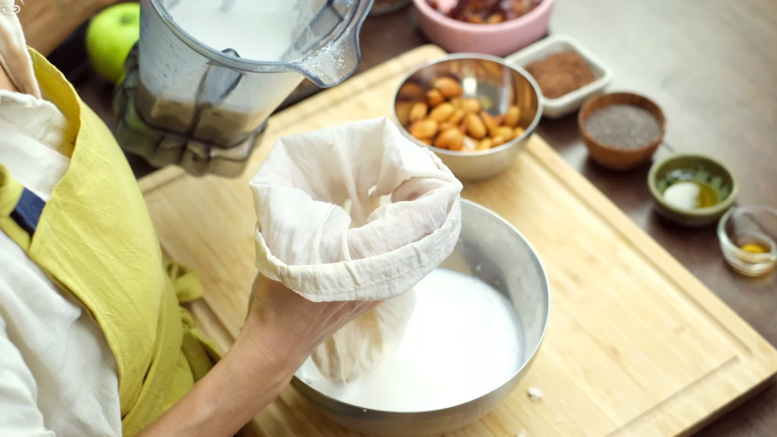 Woman squeezing almond milk from almond in kitchen at home   Royalty-Free Stock Footage #1057157143